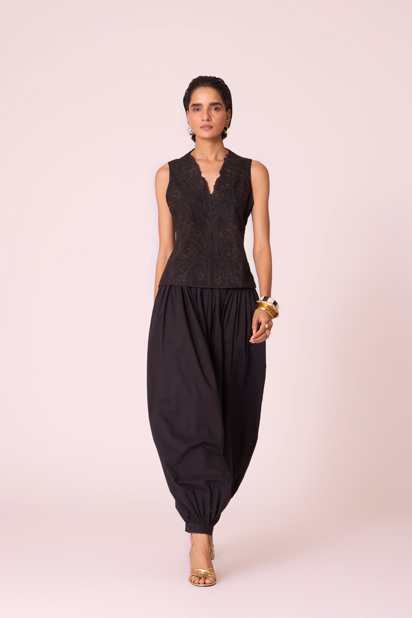 Black organic cotton pleated pants with a relaxed fit, side zip fastening, and adjustable hem cuffs.
