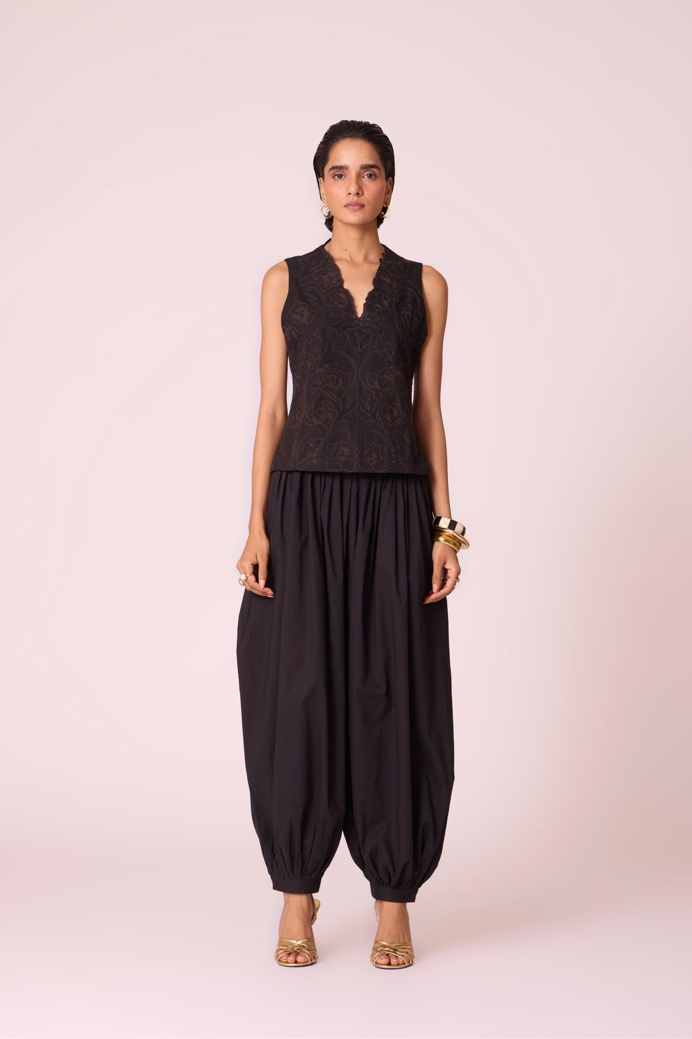 Black organic cotton pleated pants with a relaxed fit, side zip fastening, and adjustable hem cuffs.
