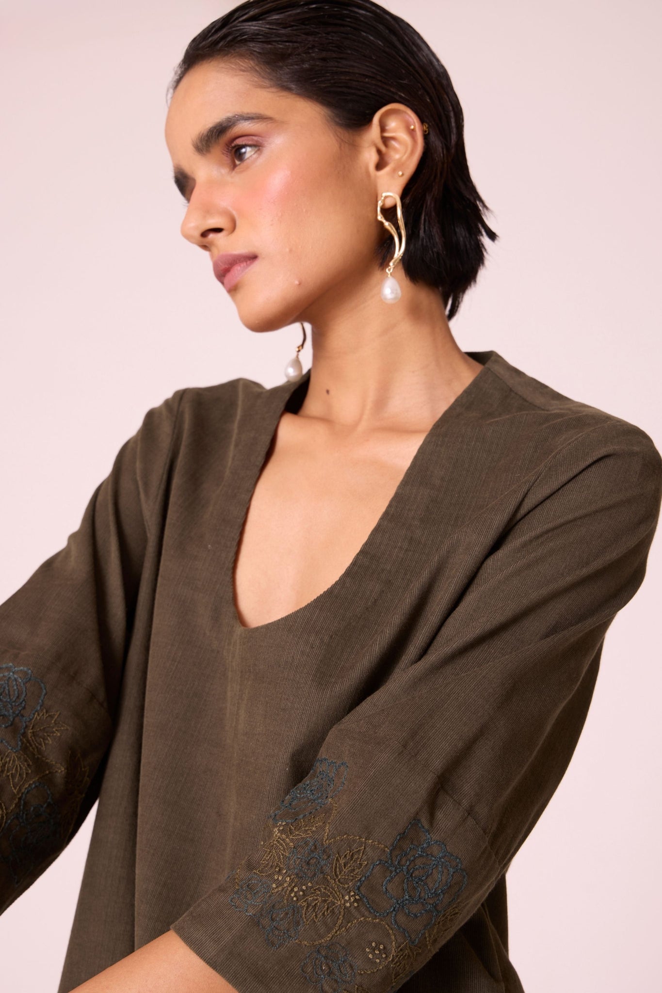 Olive needlecord A-line dress with drop shoulder, hand-embroidered cuff, deep scoop neckline, and in-seam pockets.