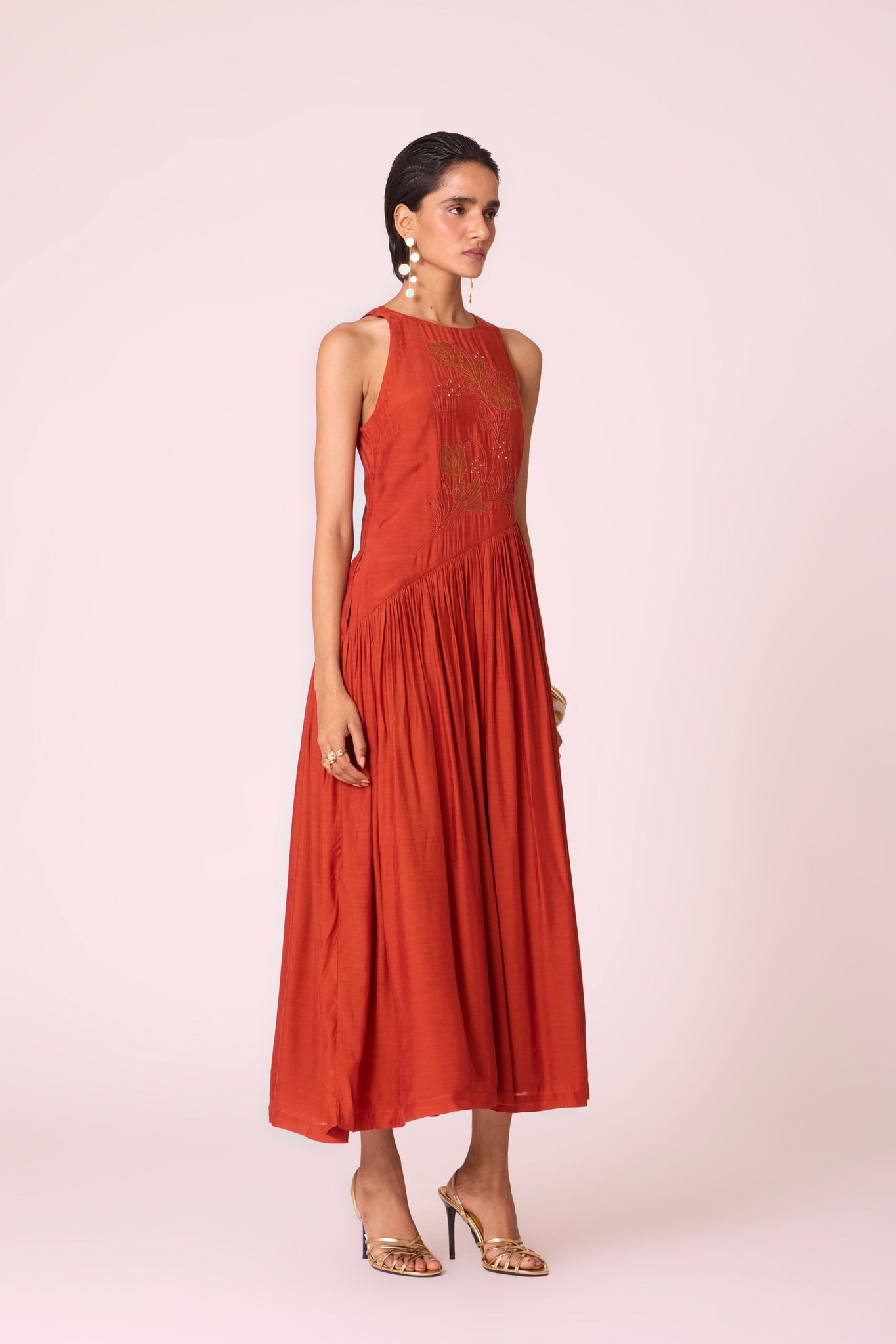 Rust cupro midi dress with hand-embroidered bodice, asymmetric gathered waist, and rouleau back button.
