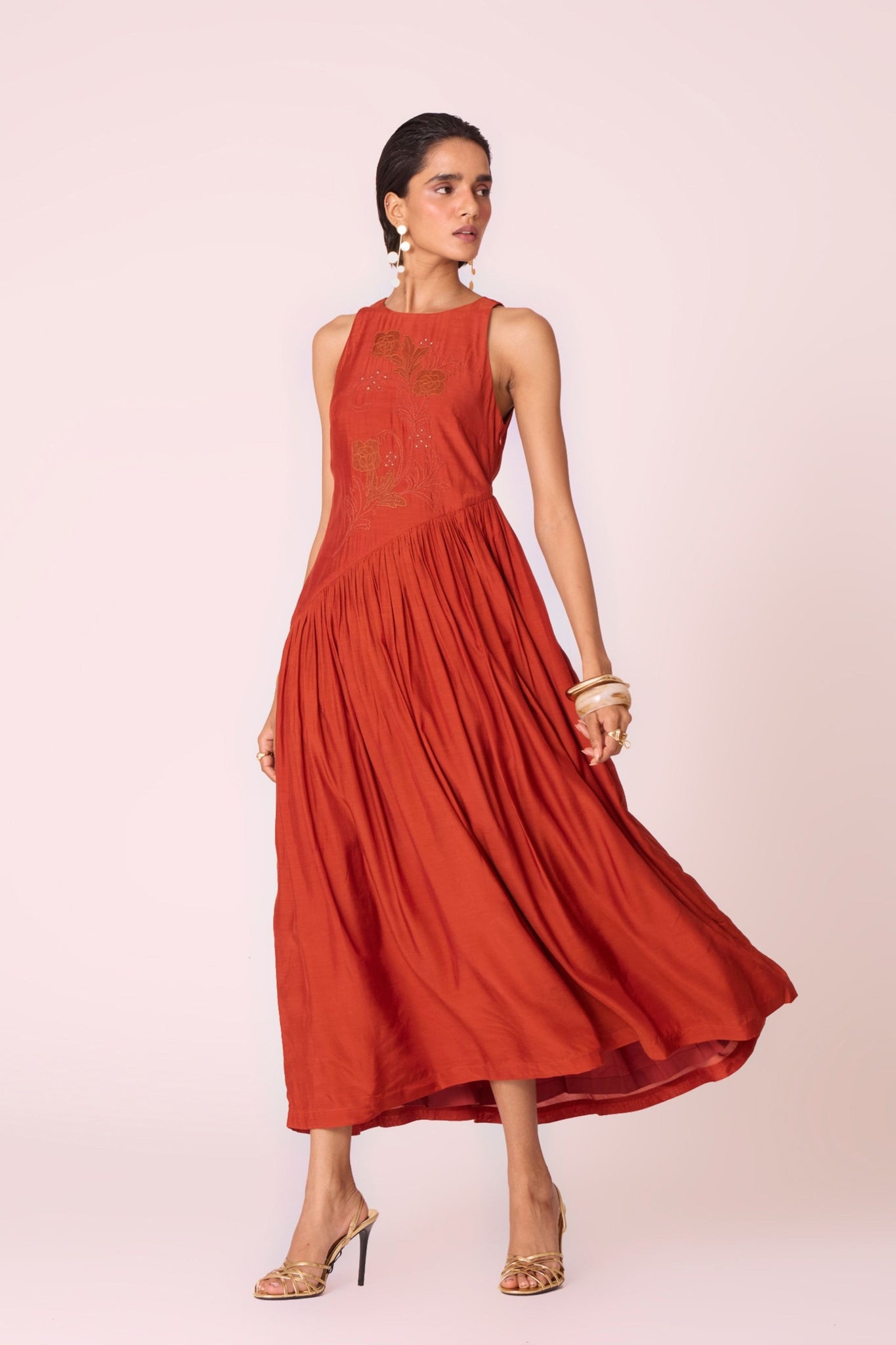 Rust cupro midi dress with hand-embroidered bodice, asymmetric gathered waist, and rouleau back button.
