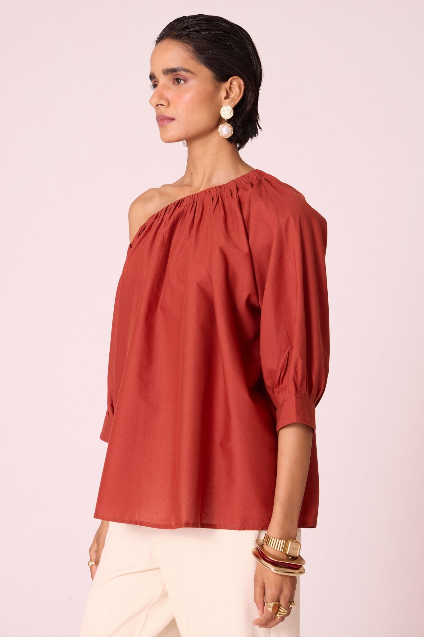 Rust organic cotton off-shoulder top with gathered neckline and pleated sleeve cuffs.