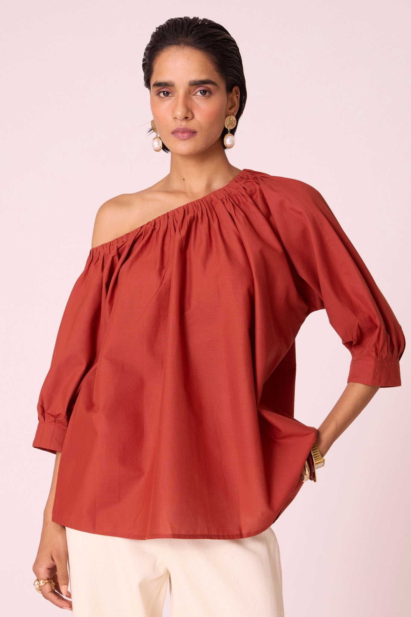 Rust organic cotton off-shoulder top with gathered neckline and pleated sleeve cuffs.