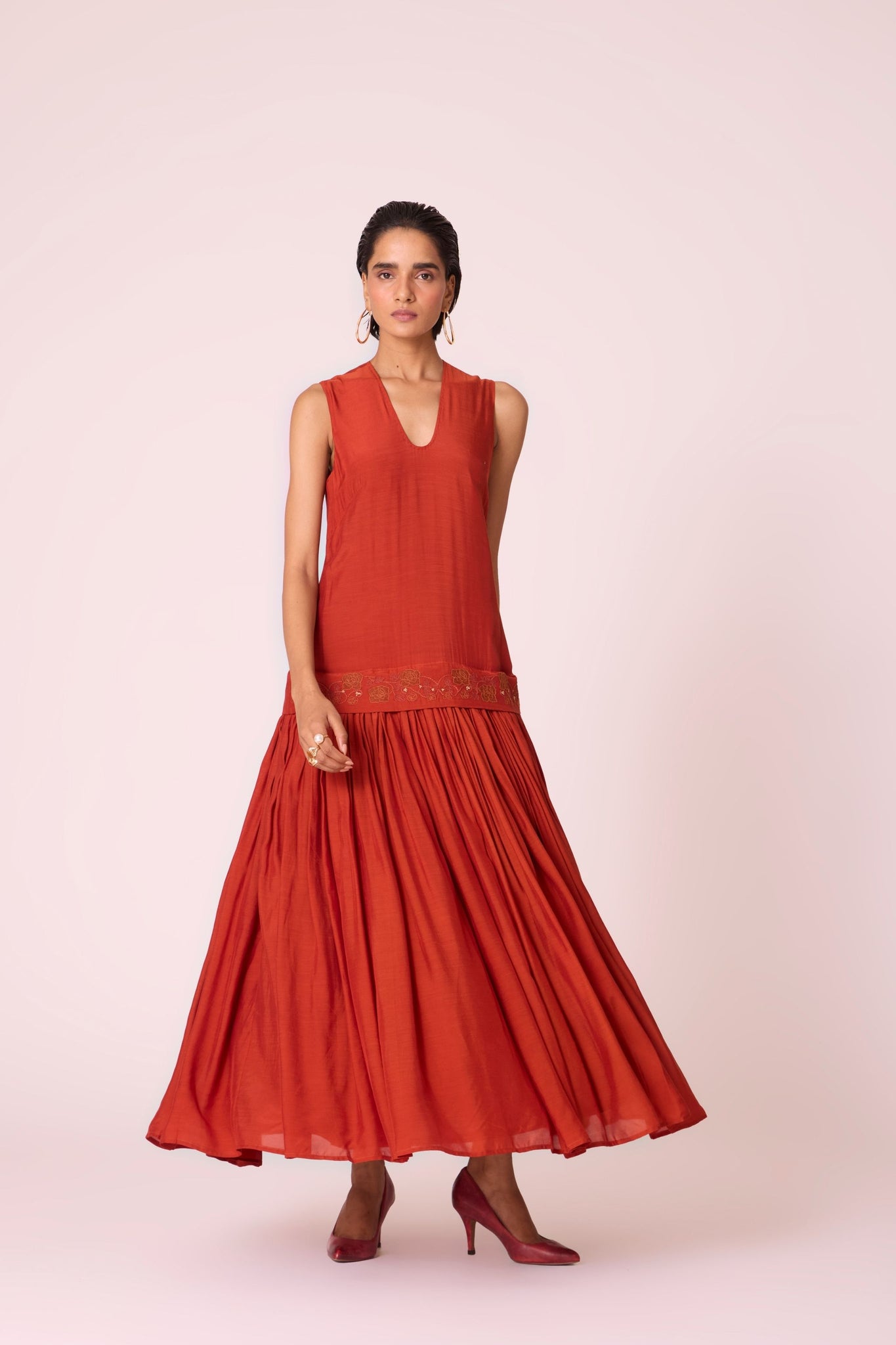 Rust cupro drop-waist dress with hand-embroidered waist, narrow scooped neckline, and full lining.
