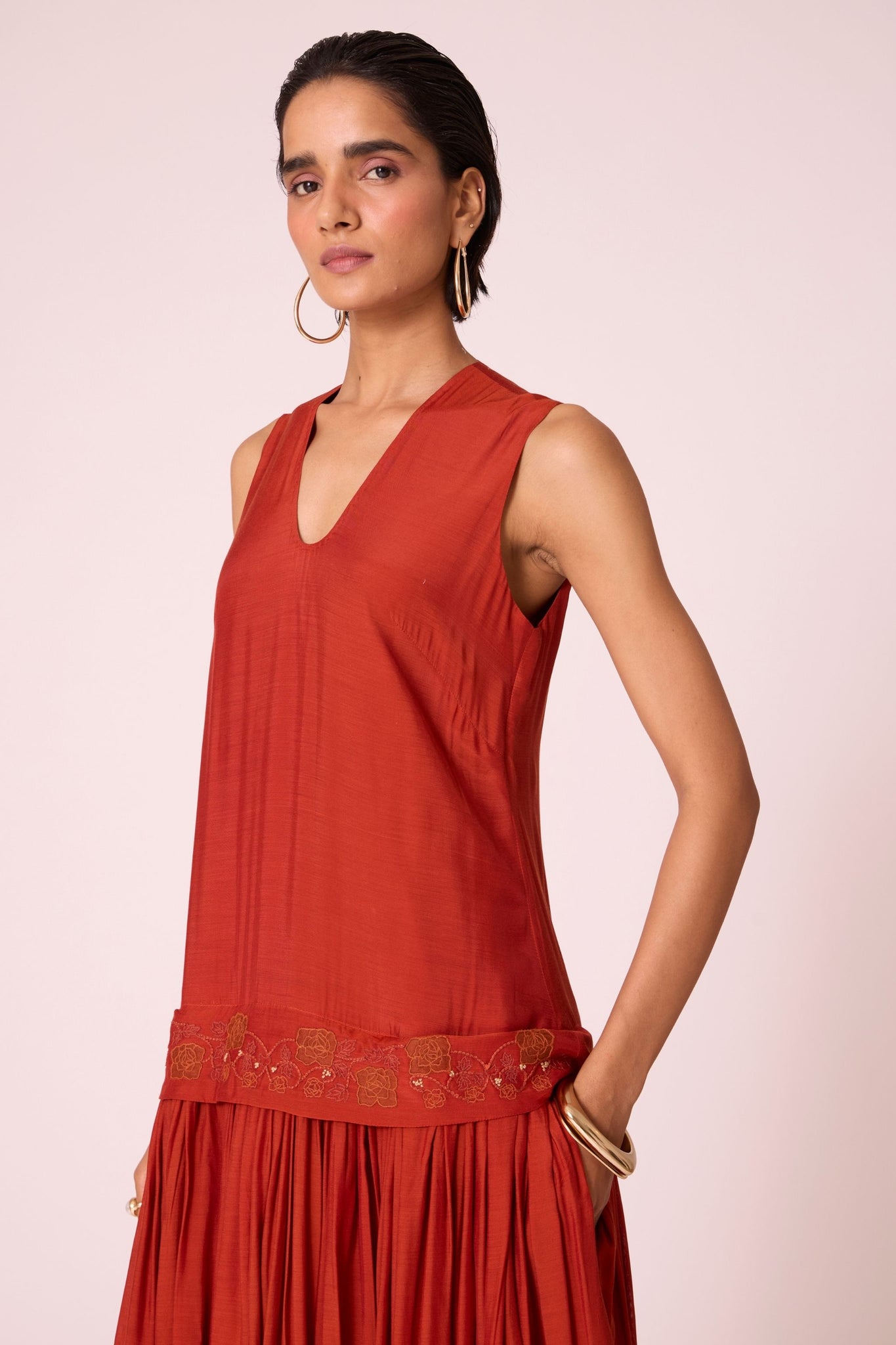 Rust cupro drop-waist dress with hand-embroidered waist, narrow scooped neckline, and full lining.
